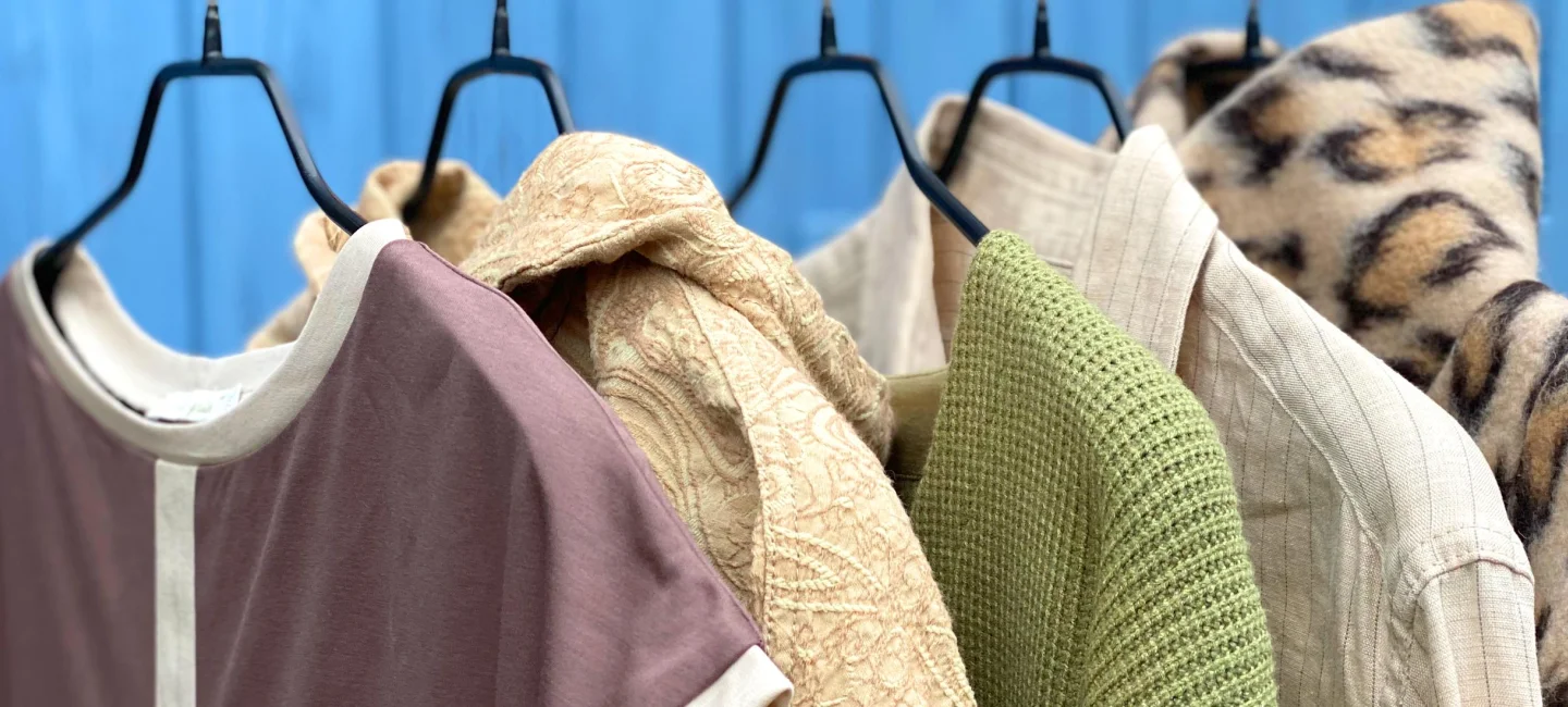 Kleidungsstücke die auf Bügeln nebeneinander hängen vor blauem Hintergrund