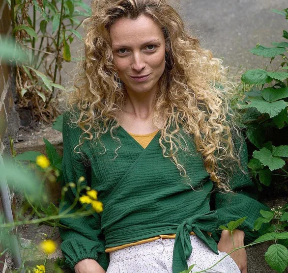Frau mit langen lockigen, blonden Haaren trägt grünes Wickeloberteil aus Musselin-Stoff